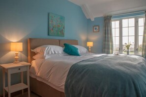 Un dormitorio con una cama, dos mesitas de noche, una ventana con cortinas y un cuadro en la pared.