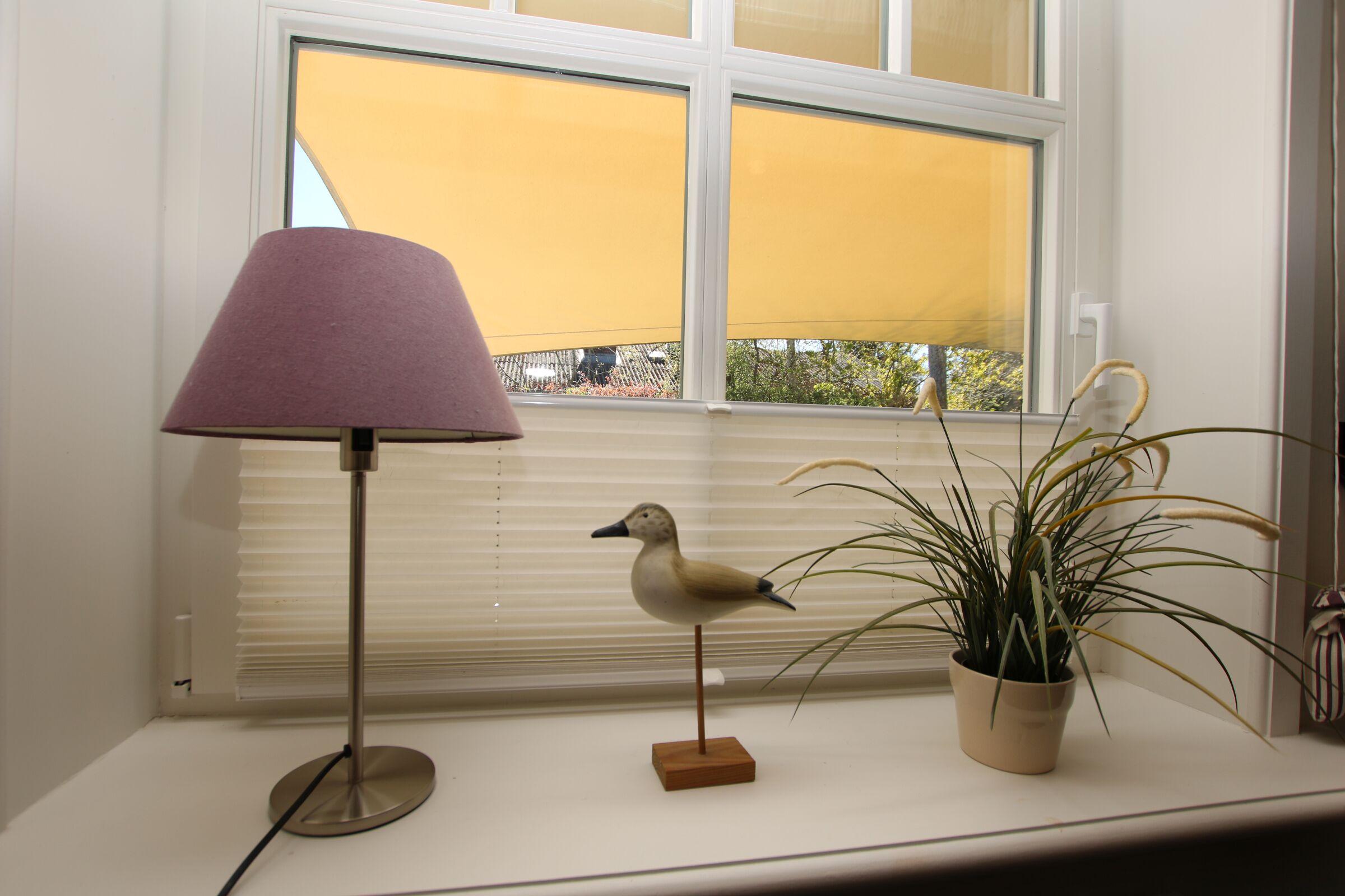 Een lamp, een vogelbeeldje en een plant in een potje op een vensterbank.