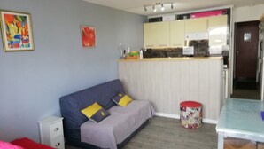 Habitación pequeña con sofá, un archivador blanco, cama roja y una zona de kitchenette con armarios y encimera.