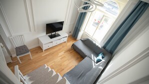 A modern bedroom with a bed, a TV on a white dresser, and a window with curtains.