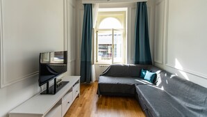 A modern living room with a flat-screen TV, a sofa, and a window with curtains.