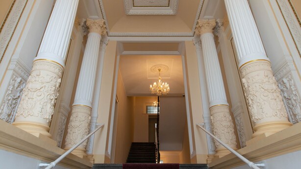 A grand staircase with marble columns and a chandelier.