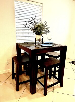 Uma mesa de jantar com quatro cadeiras, um vaso de flores e dois copos de vinho.