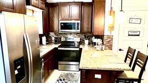 Una cocina con armarios de madera oscura, electrodomésticos de acero inoxidable, encimera de granito y alfombra estampada.