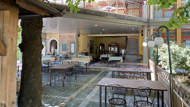 An outdoor café with tables and chairs, a Coca-Cola refrigerator, and a sign indicating the café is open.