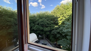 A window with a view of a courtyard with trees and a white structure.