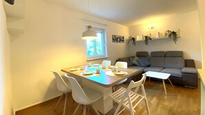 A modern living room with a dining area, a grey sofa, and a wooden floor.