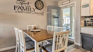 A dining area with a wooden table and white chairs, a clock, and a welcome sign on the door. - Pool Access, Near Beach! Waterfront Ocean City Gem (Ocean City)
