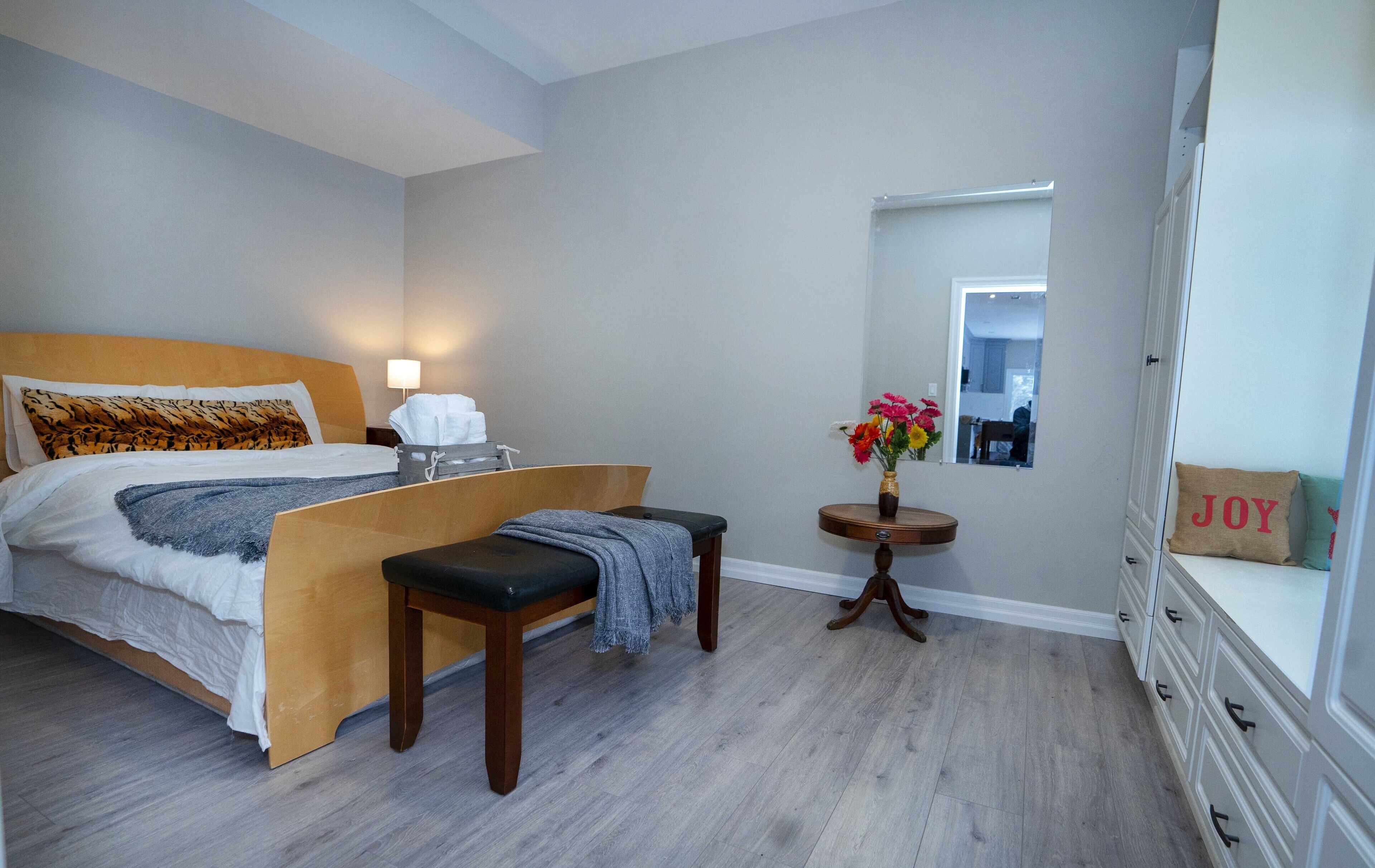 Ein Schlafzimmer mit Bett, Nachttisch, Bank und einem kleinen Tisch mit Blumenvase.