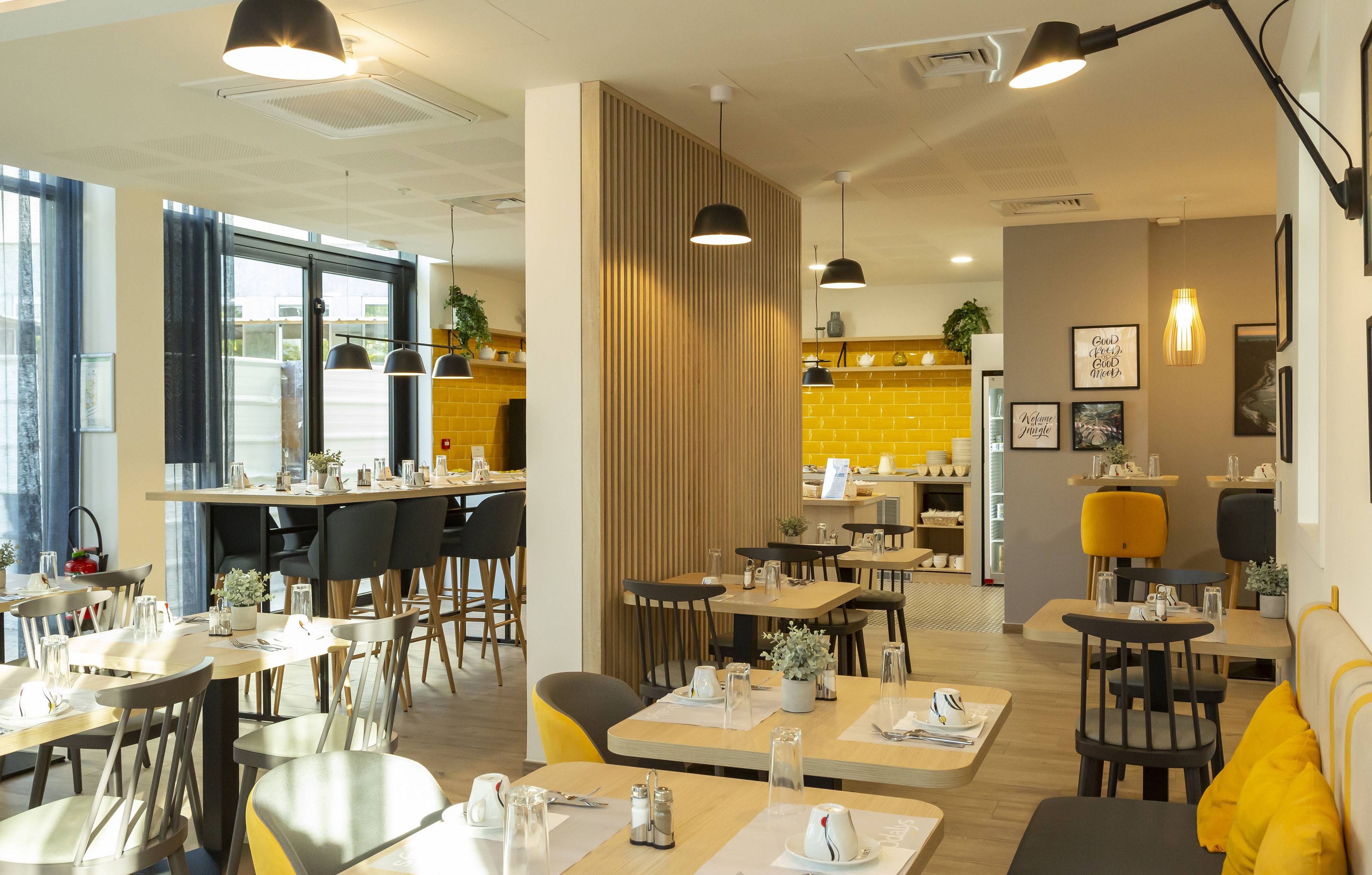 A modern restaurant with wooden tables and chairs, pendant lighting, and a yellow accent wall.