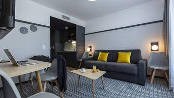 Ein modernes Hotelzimmer mit einer Couch, einem Esstisch, einem Laptop und einem kleinen Couchtisch.