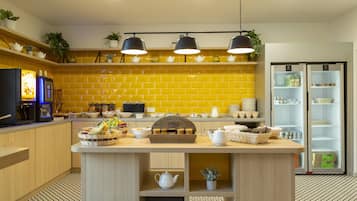 Eine moderne Küche mit gelben Fliesen, einer zentralen Kochinsel mit Teeservice, einer Kaffeemaschine und einem Kühlschrank.
