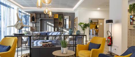 Un espacio de sala moderno con un sofá, sillas amarillas, una mesa de centro y una cocina al fondo.