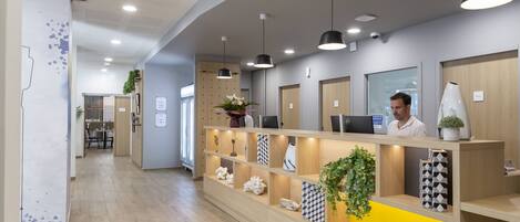 A reception area with a wooden reception desk, multiple pendant lights, and shelves with decorative items.