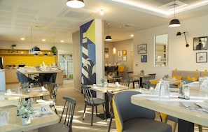 A modern restaurant interior with multiple dining tables, chairs, and pendant lighting.