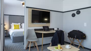 Habitación de hotel con cama, escritorio con una computadora portátil, silla, mesa con desayuno y maleta.