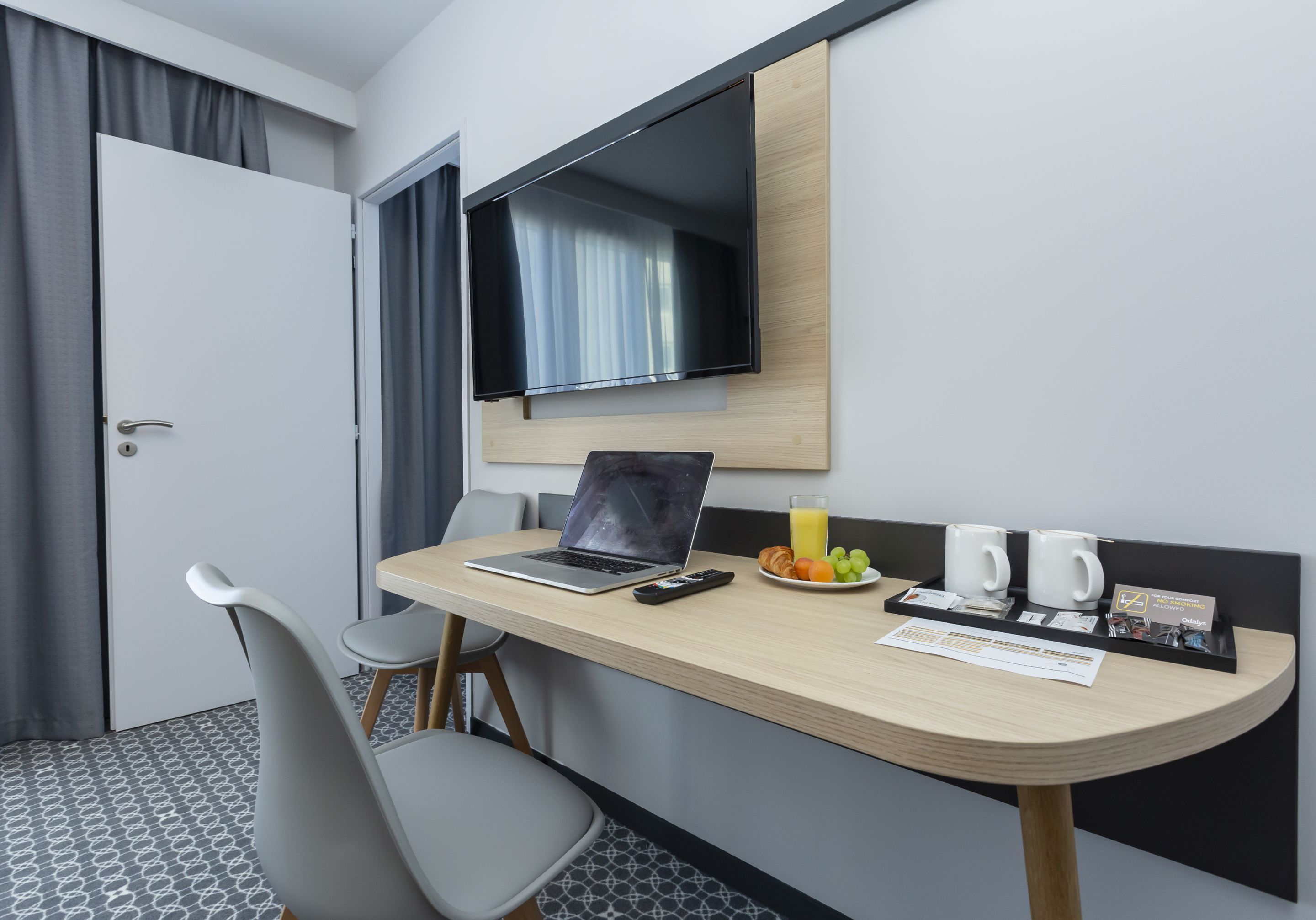 A hotel room with a desk, a laptop, a TV, a chair, a breakfast tray, and a bed.