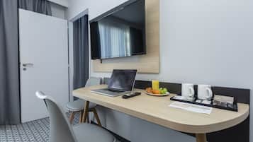 A hotel room with a desk, a laptop, a TV, a chair, a breakfast tray, and a bed.