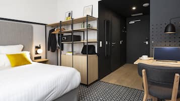 Ein modernes Hotelzimmer mit Bett, Schreibtisch mit Laptop, Kleiderschrank und einer kleinen Sitzecke.
