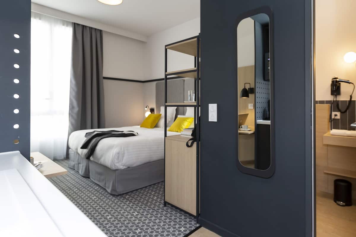 A modern hotel room with a bed, bedside table, and a large mirror.