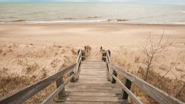 Une promenade en bois mène à une plage de sable, avec l’océan en arrière-plan.