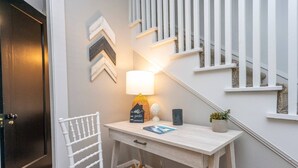 Une petite pièce bien éclairée, avec un bureau, une chaise et un escalier doté de rampes blanches.