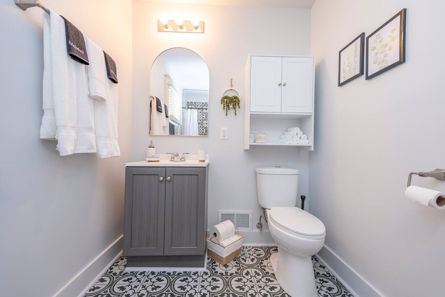 Un baño con tocador gris, inodoro blanco y baldosas de suelo estampadas.