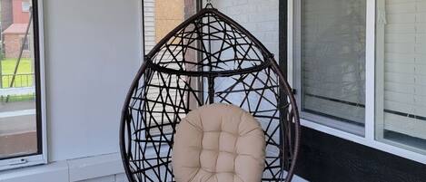 Una silla colgante con asiento acolchado en una habitación con suelo de baldosas y ventanas amplias.