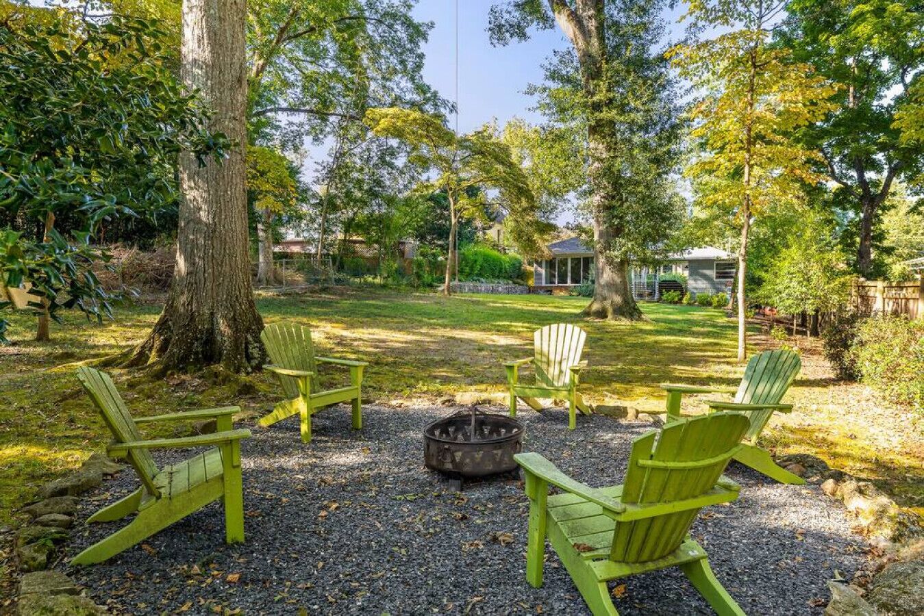 Un cortile con un braciere, quattro poltrone Adirondack verdi e un albero grande.