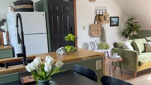 A modern kitchen with a white refrigerator, a wooden countertop, and a dining table with chairs. There is a vase with white flowers on the table.