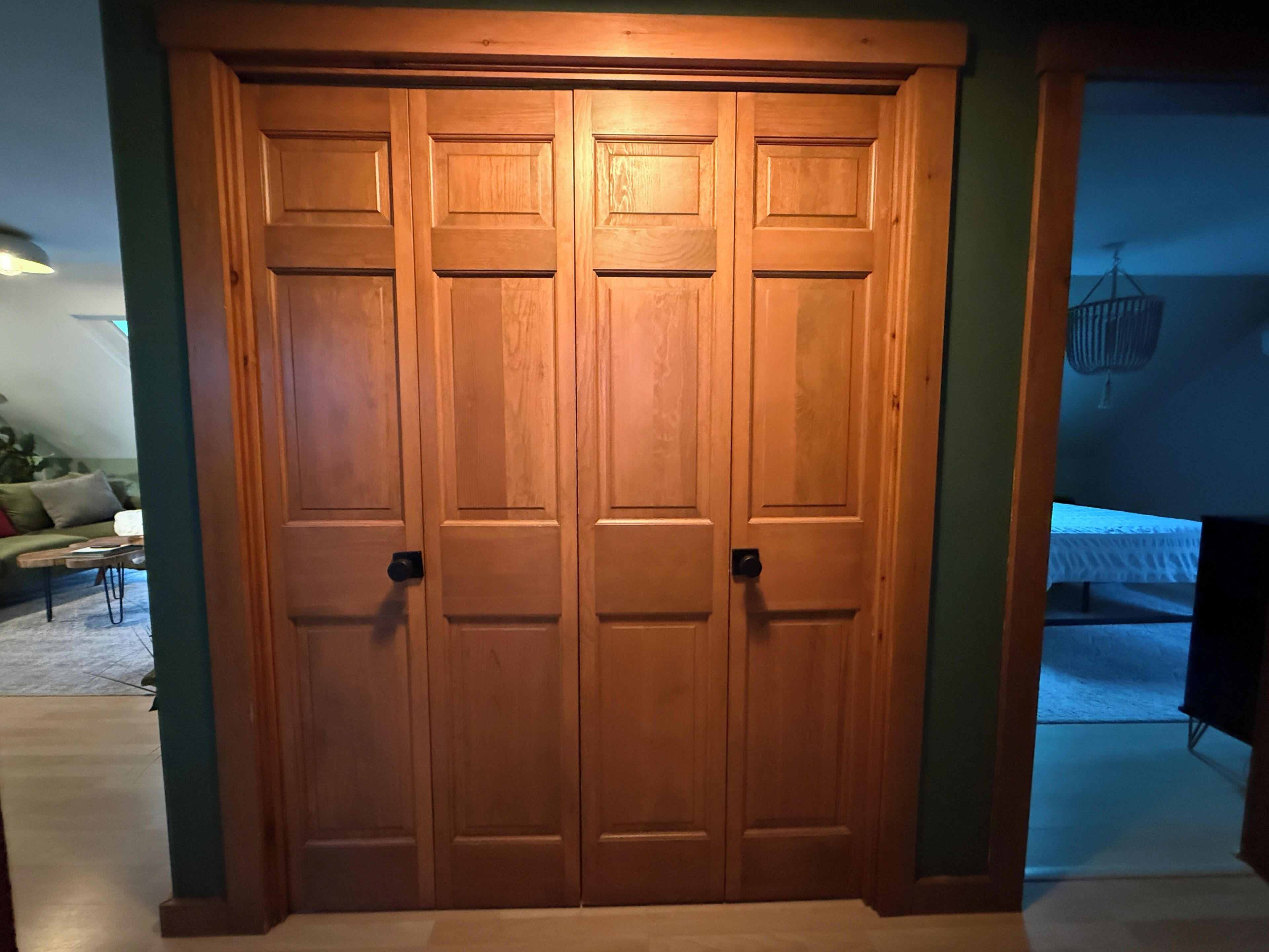 Une porte double en bois, au design simple, qui donne sur une pièce comprenant un lit et un luminaire suspendu.