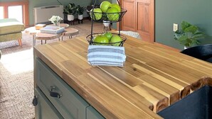 A modern kitchen with a wooden countertop, a hanging light fixture, and a fruit basket.