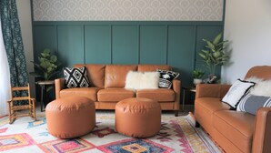 A living room with a teal accent wall, a brown leather sofa, two ottomans, and a colorful patterned rug. - Unleash Your Inner Explorer: The Dam Dino House! (Page)