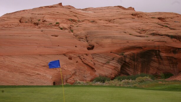 A golf course with a flag on a green, a red rock formation in the background. - Unleash Your Inner Explorer: The Dam Dino House! (Page)