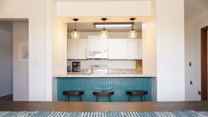 A kitchen with white cabinets, a blue accent wall, a microwave, and three bar stools. - Unleash Your Inner Explorer: The Dam Dino House! (Page)