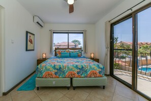 A bedroom with a bed, a window, a ceiling fan, and a view of a swimming pool.