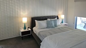 Hotellihuone, jossa on sänky, kaksi yöpöytää, yölamppu, kuvioitu seinä ja ikkuna, josta on näkymä.
