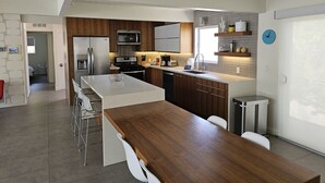 Moderni keittiö, jossa on puiset kaapit, ruostumattomasta teräksestä valmistetut kodinkoneet ja keskellä sijaitseva saareke, jonka ympärillä on baarituoleja.