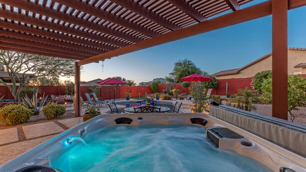 Un espace avec un jacuzzi, surmonté d’une pergola, entouré de mobilier de jardin et de parasols.