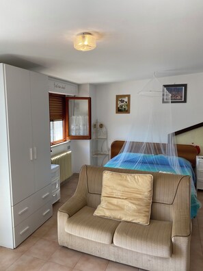 A bedroom with a bed under a mosquito net, a sofa with a cushion, a wardrobe, a radiator, and a ceiling light. - The attic of Podere Bellavista (Monteprandone)