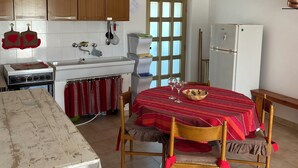 Een keuken met houten kastjes, een fornuis, een spoelbak en een eettafel met stoelen.