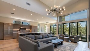 A modern open-plan living area with a large grey sectional sofa, a coffee table, and a dining area with a kitchen in the background. - Larkspur Luxe - Northstar- 4 BR w Pool, Gym, Access - Walk to Village. Hot Tub! (Truckee)