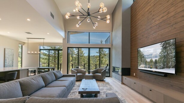 A spacious living room with a large sectional sofa, a coffee table, and a flat-screen TV mounted on a wooden wall. - Larkspur Luxe - Northstar- 4 BR w Pool, Gym, Access - Walk to Village. Hot Tub! (Truckee)