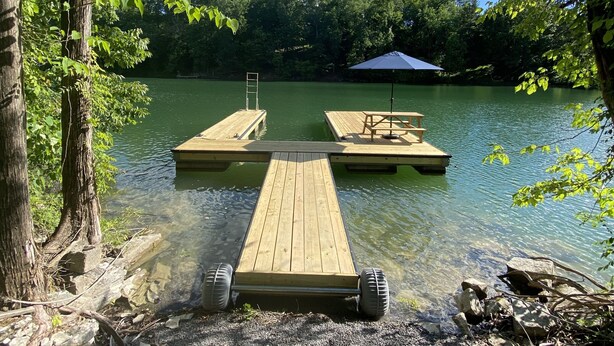 Un muelle de madera que se adentra en un lago, rodeado de árboles y un cielo despejado.