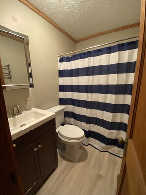 Un baño con un lavabo blanco, muebles de madera oscura, un inodoro blanco y una cortina de ducha a rayas azul y blanco.