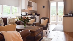 A spacious living area with a sofa, armchairs, and a coffee table. There is a kitchen area with cabinets and a microwave. A large window provides a view of the outdoors. - 3 bedroom accommodation in Aberfoyle (Aberfoyle)