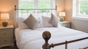 A neatly made bed with white linens and two pillows, flanked by nightstands with lamps, in a room with large windows offering a view of greenery. - 3 bedroom accommodation in Aberfoyle (Aberfoyle)