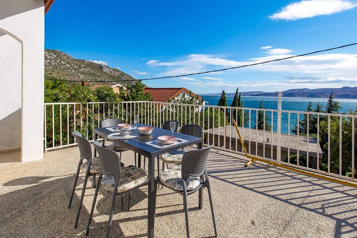 A terrace with a table set for four, overlooking a scenic lake and mountains.