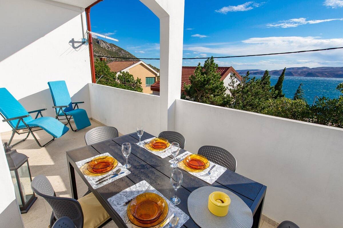 A terrace with a table set for dining, overlooking a scenic landscape with houses and a body of water.