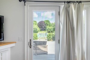A door with a view of a garden, a wicker chair, and a television on a stand.